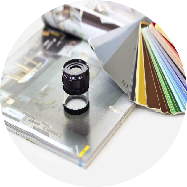 Typisches Bild aus dem Printbereich: Eine Lupe steht auf einer Seite eines Kataloges. Rechts sieht man einen Farbfächer. Wenn man auf das Bild klickt, kommt man zum Thema Printdesign.