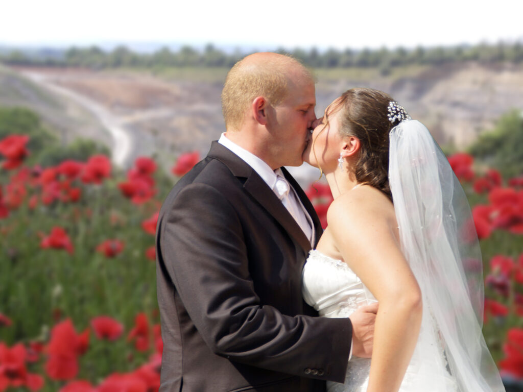 Ein Brautpaar küsst sich vor dem Hintergrund eines Mohnfeldes